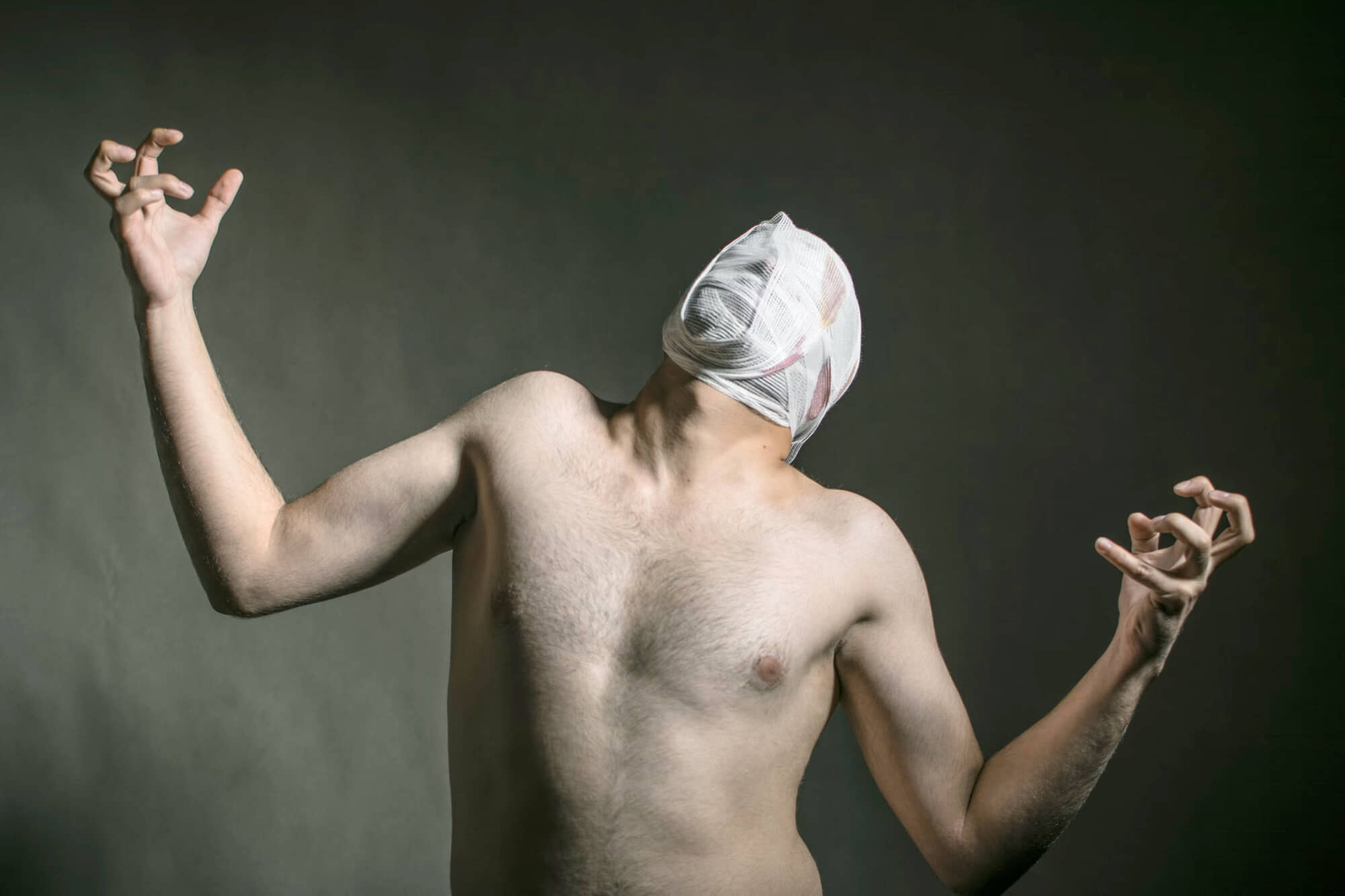 shirtless man from the stomach up with gauze over his face.