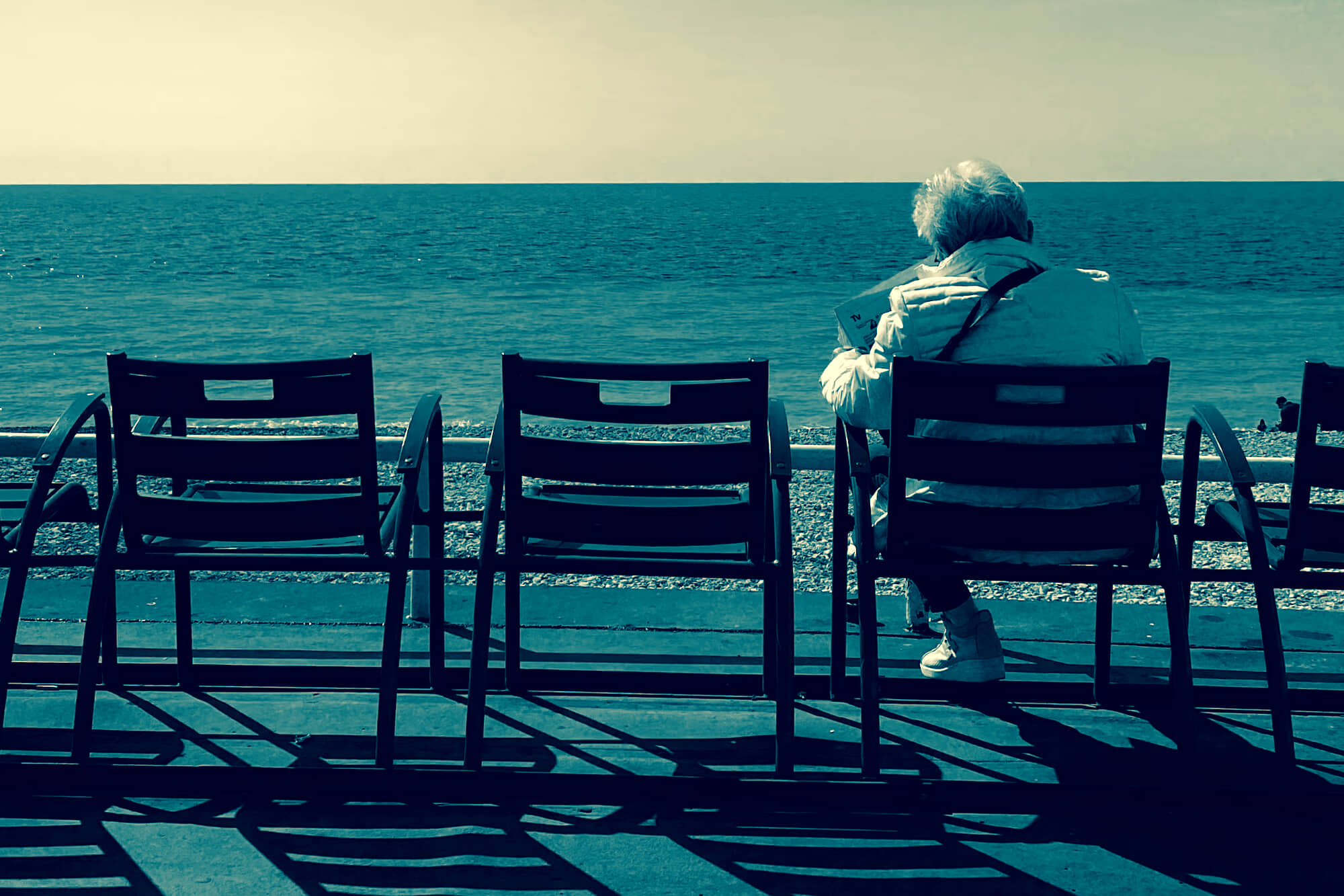 a person sits facing away from the camera, looking at a paper in front of a body of water