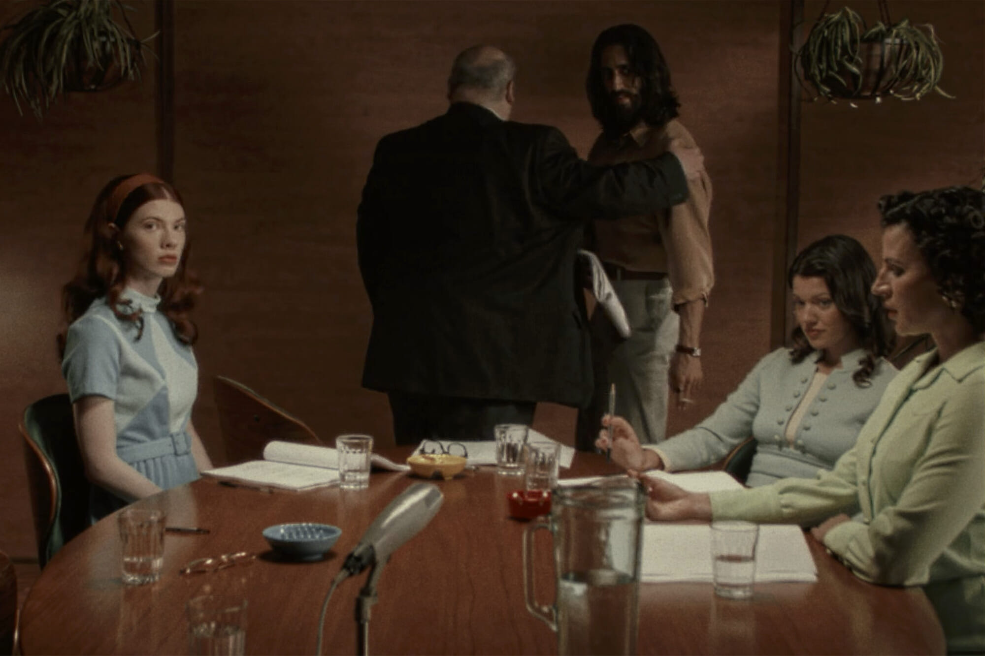 three women sitting at a desk while two men are in the background